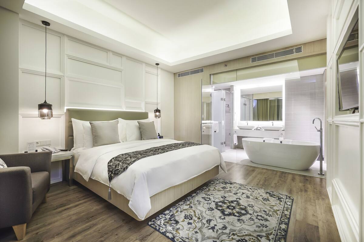 Une chambre d’hôtel moderne dotée d’un grand lit, d’un coin salon, d’une baignoire et d’une douche à l’italienne.