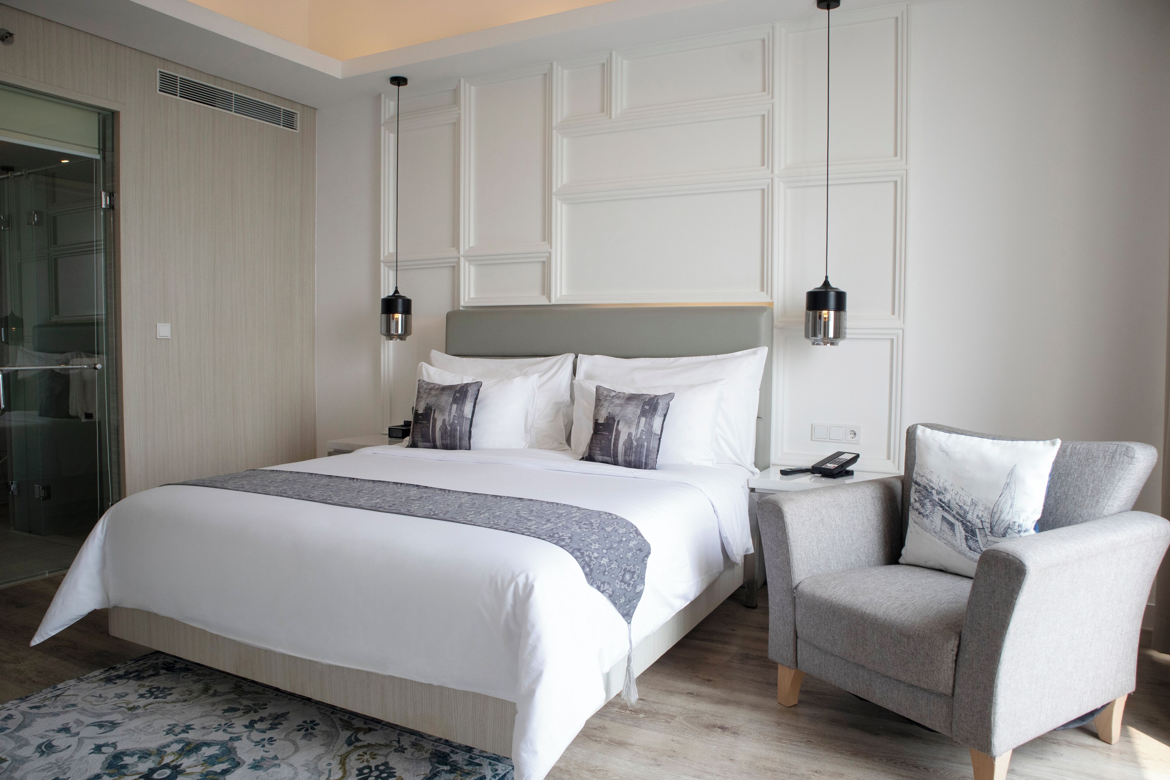 A modern bedroom with a large bed, a grey armchair, and a bedside table with a lamp.