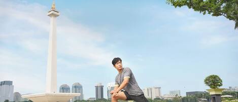 A person stretching in an open area with a monument and buildings in the background.