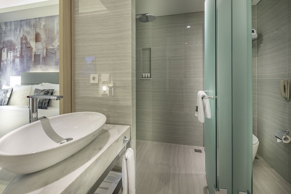 A modern bathroom with a large white sink, a glass shower enclosure, and a toilet.