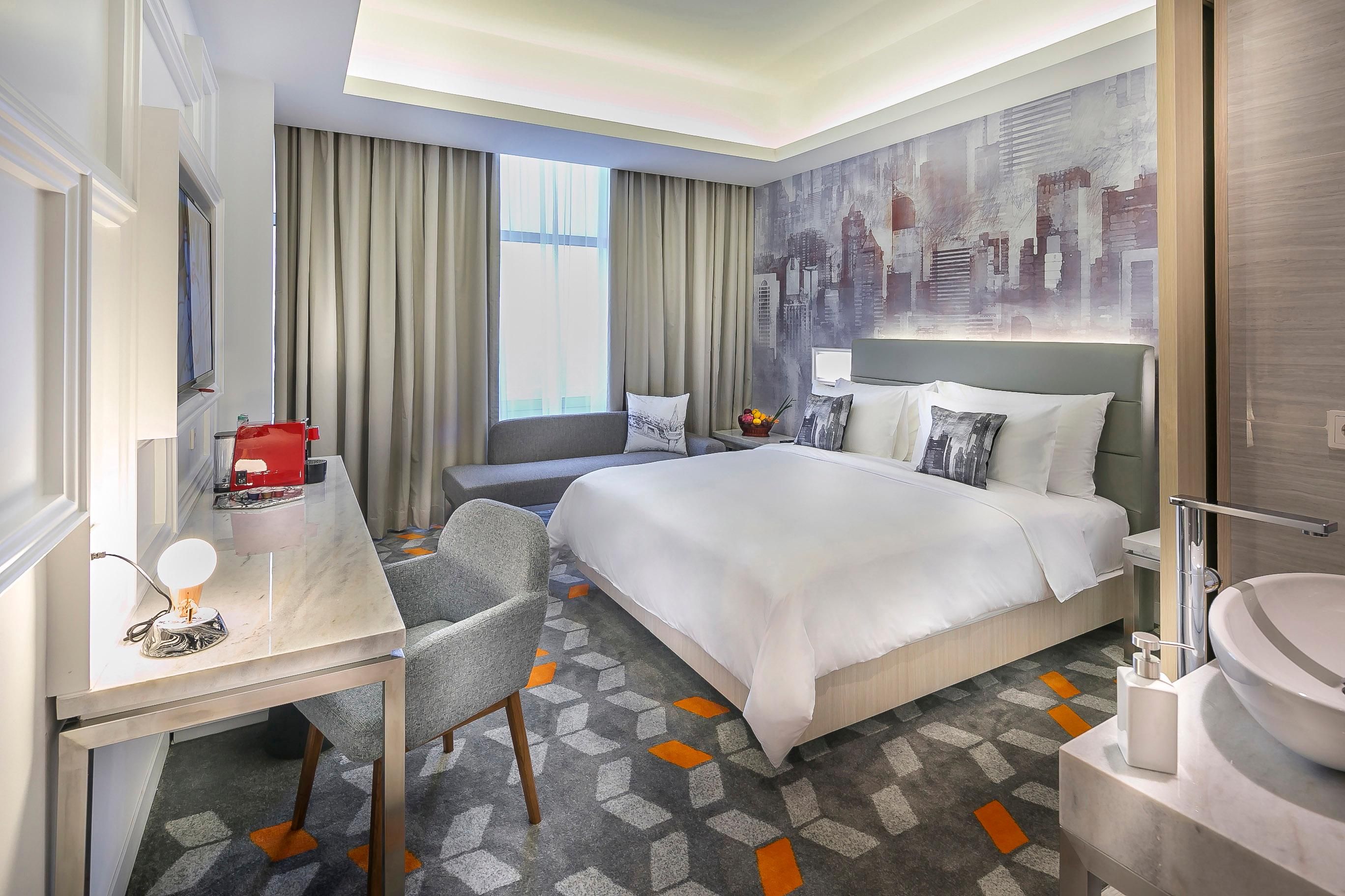A hotel room with a bed, a desk, a chair, a bathroom, and a cityscape mural on the wall.
