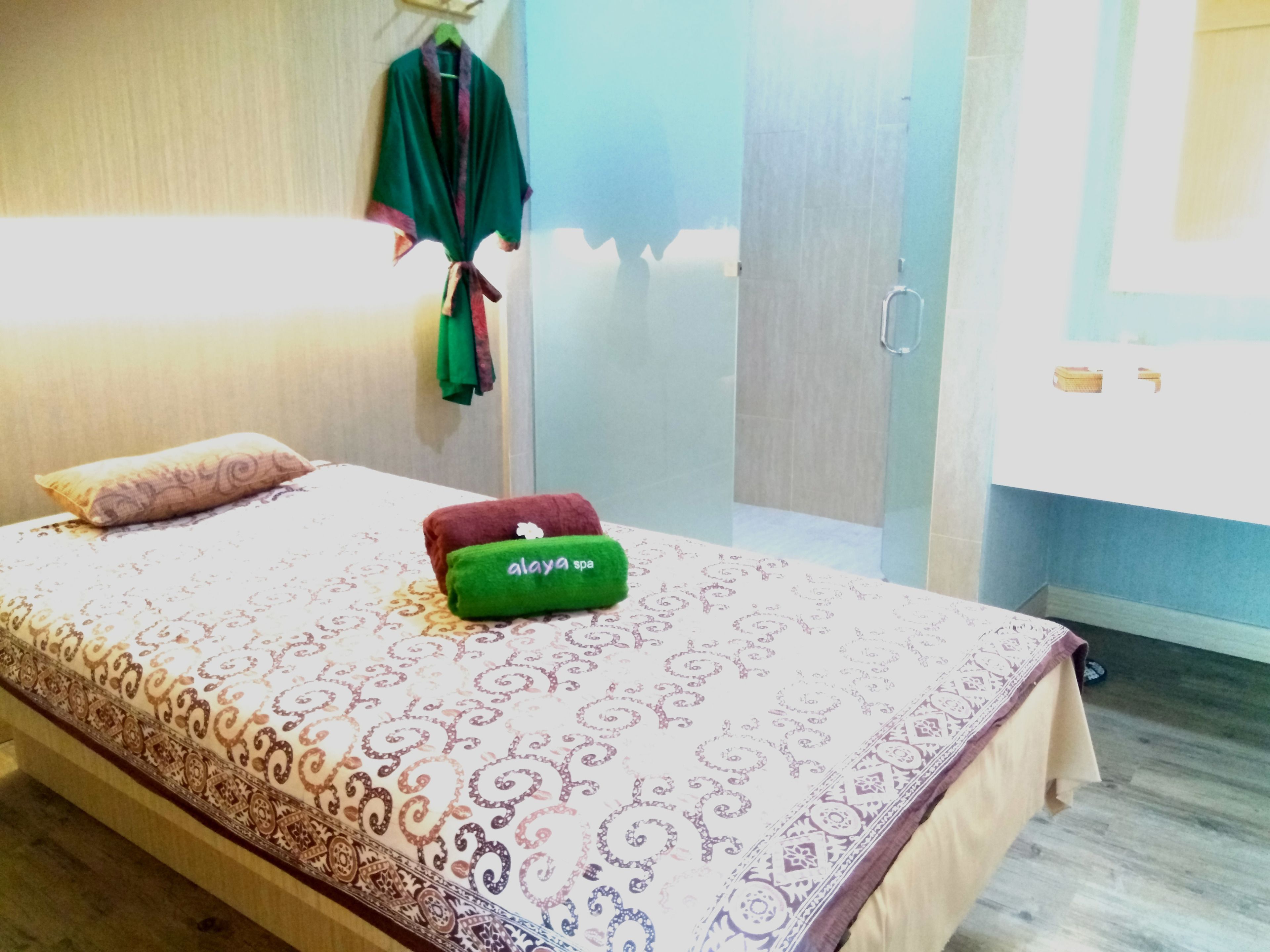 A hotel room with a bed, a green and red towel, and a patterned bedspread.