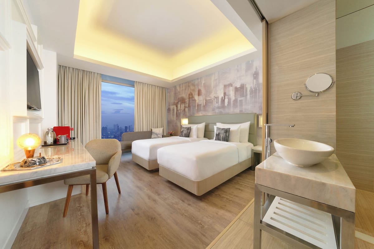 Une chambre d’hôtel avec un grand lit, un bureau avec une lampe, une vue sur la ville et une salle de bain avec un grand lavabo.