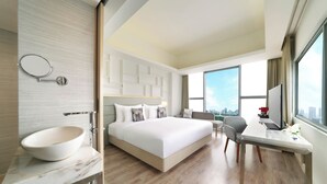 Una habitación de hotel moderna con una cama grande, un lavabo redondo, un escritorio y vistas a la ciudad.