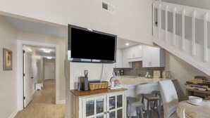 A compact kitchen with a built-in TV, a dining area with stools, and a staircase. - Eastern Shores on 30A by Panhandle Getaways (Santa Rosa Beach)