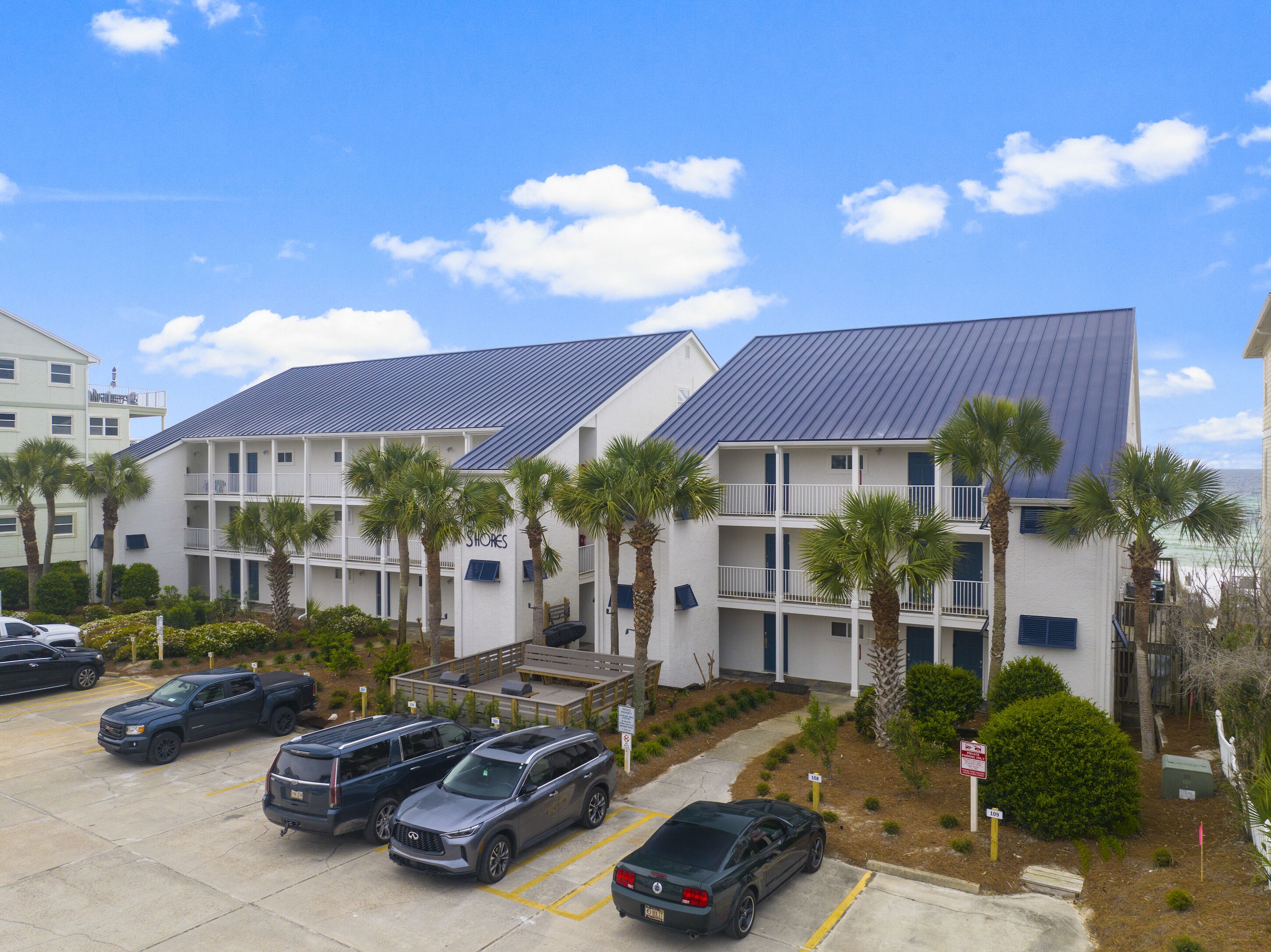 A multi-story hotel with a parking lot, palm trees, and a clear blue sky.