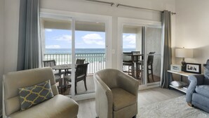 A living room with a view of the beach, a balcony with a table and chairs, and a sofa with a patterned pillow. - Eastern Shores on 30A by Panhandle Getaways (Santa Rosa Beach)