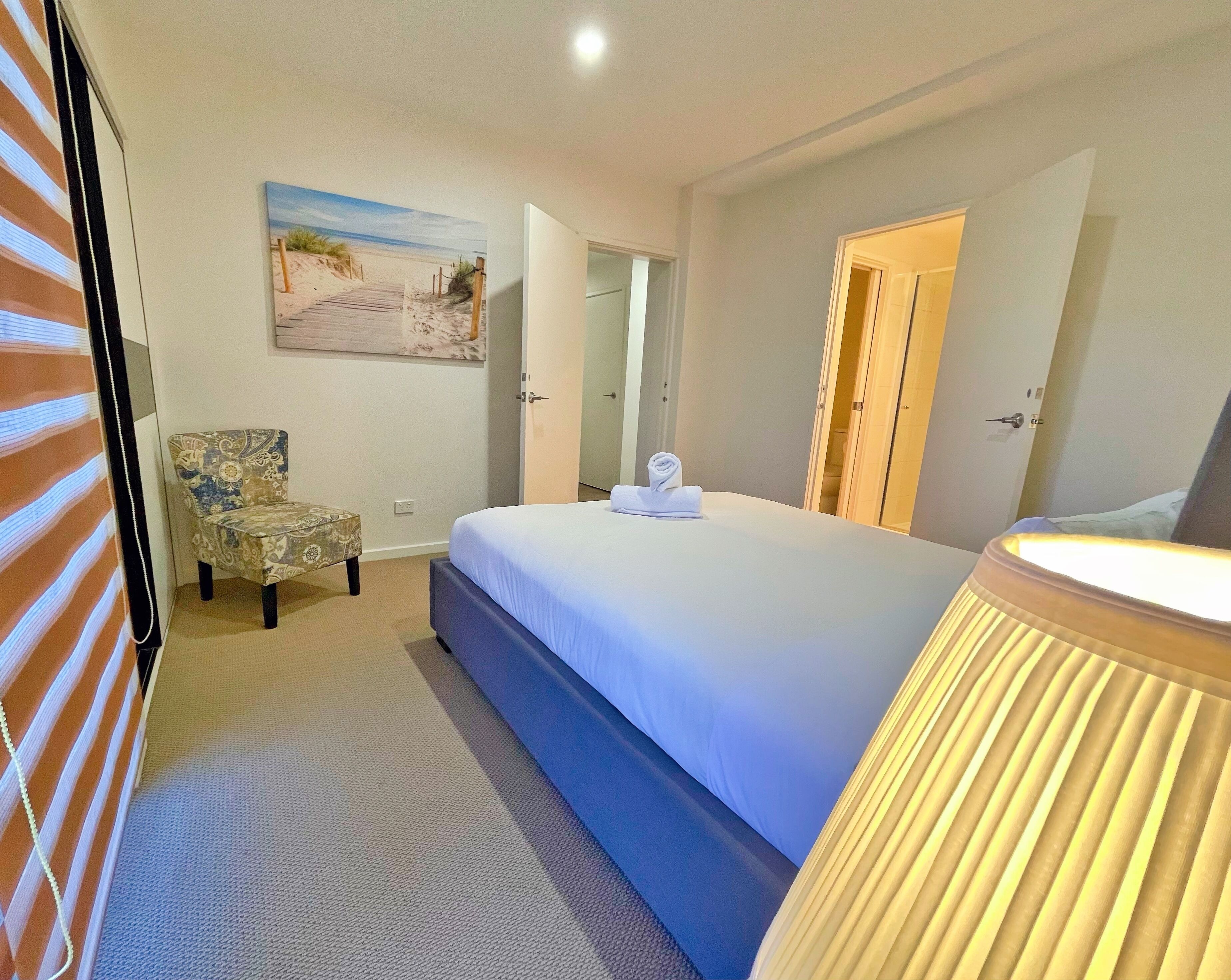 A hotel room with a bed, a chair, a painting, and a door.
