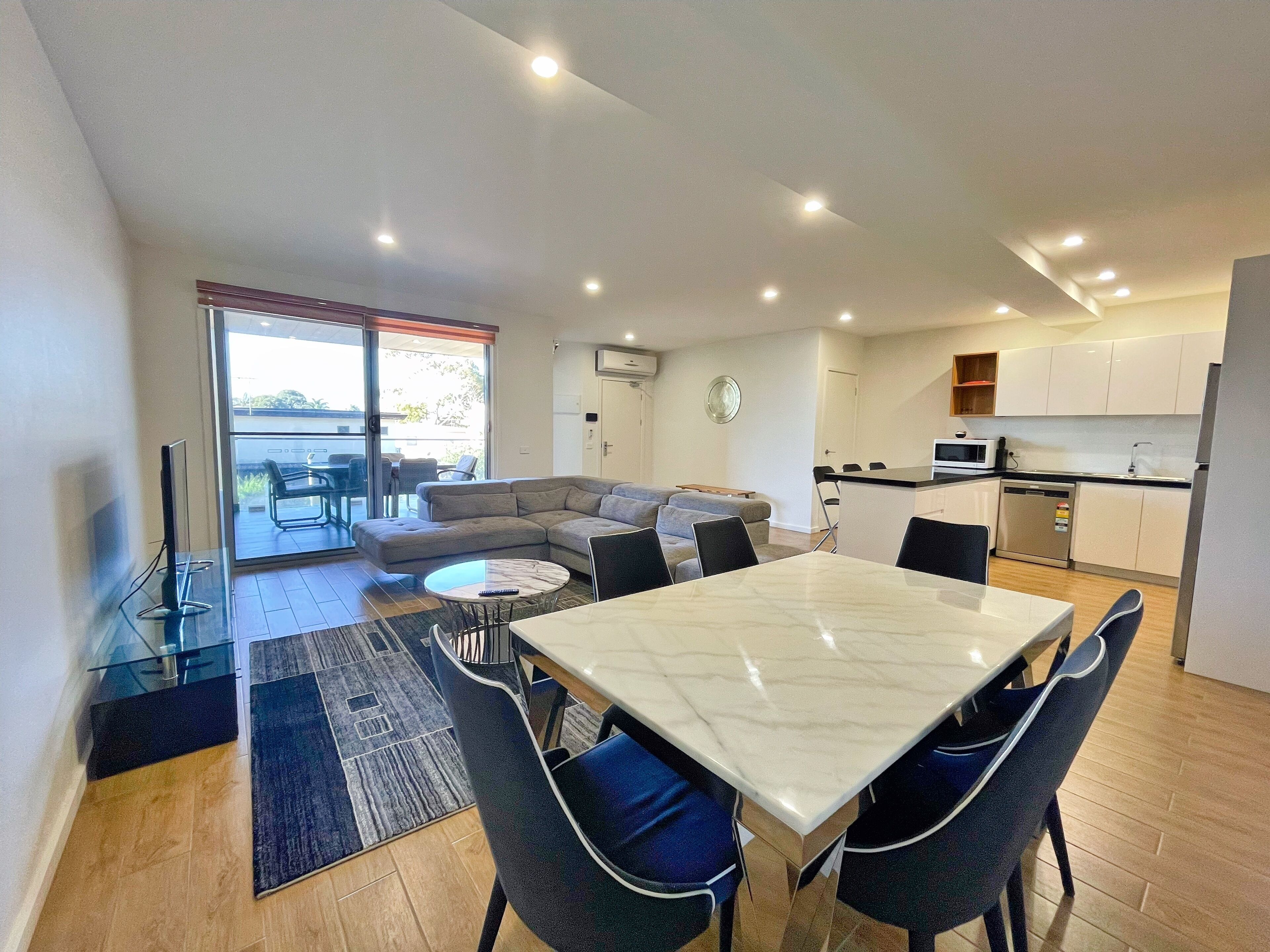 A modern apartment with a dining area, kitchen, and a living room with a sofa and a TV.