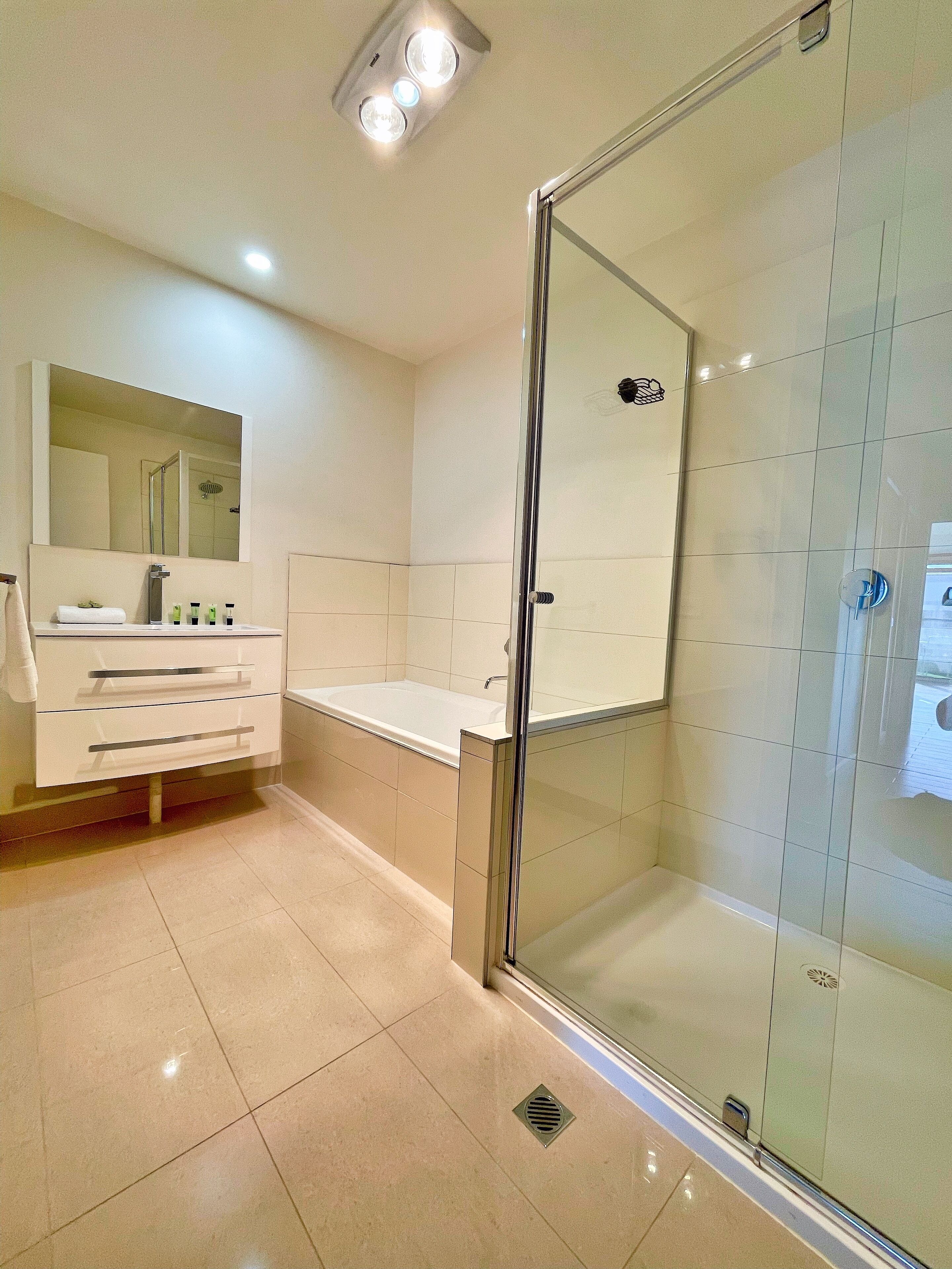 Een moderne badkamer met een douchecabine van glas, een grote spiegel en een witte wastafel met lades.