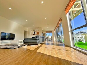 Uma sala de estar moderna com televisão de tela plana, sofá cinza e uma grande janela com vista para o exterior.