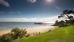 A beach with a pier extending into the water, a clear sky, and a grassy area with trees. - Phillip Island Towers (Cowes)