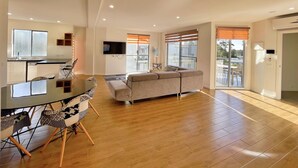 A spacious living area with a sofa, a dining table with chairs, a kitchen area with a sink and a TV mounted on the wall. - Phillip Island Towers (Cowes)