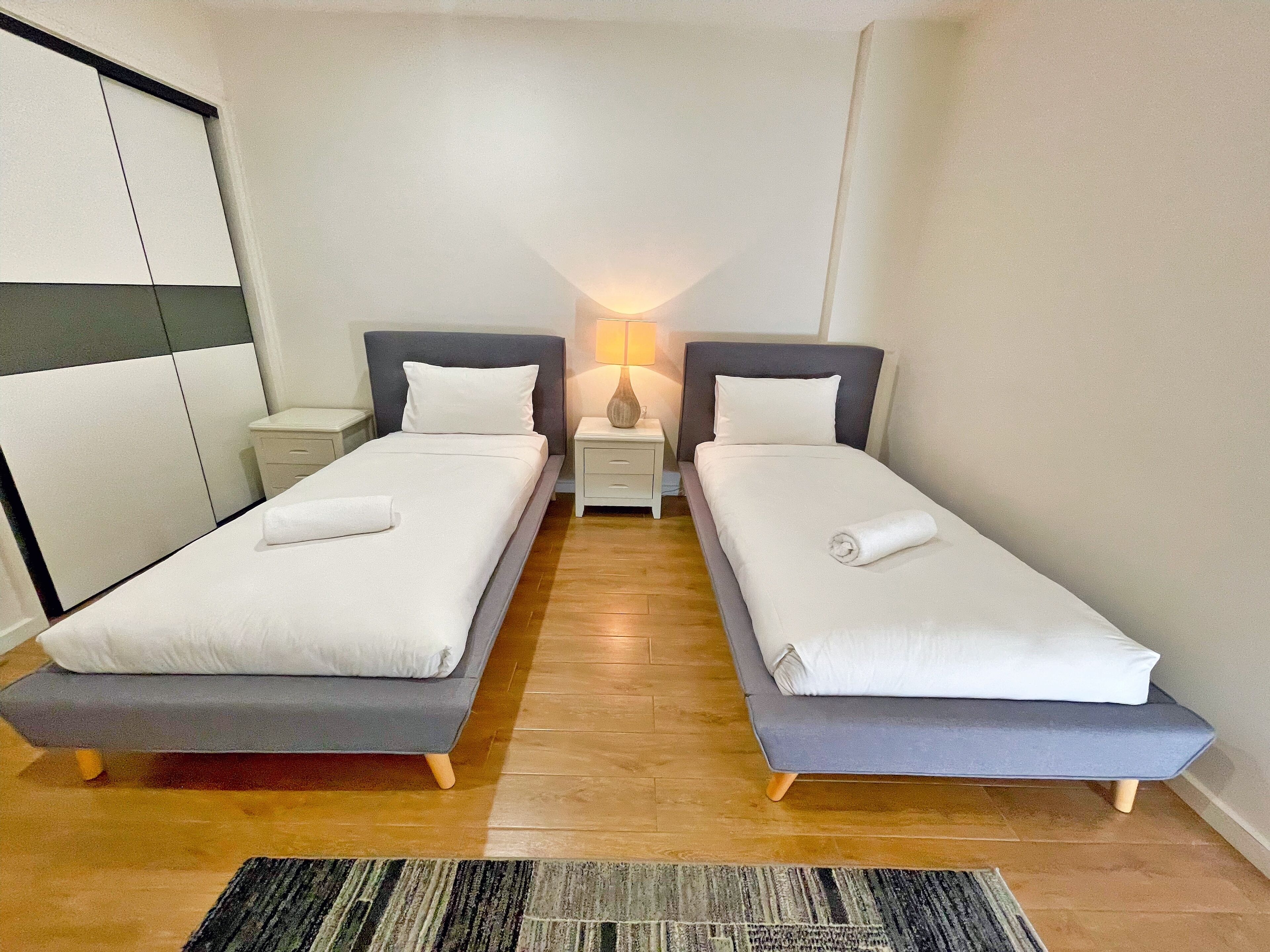 A twin bedroom with two single beds, a bedside table with a lamp, and a wooden floor.