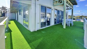 A modern building with large glass doors and windows, a covered outdoor seating area, and a green artificial lawn. - Phillip Island Towers (Cowes)