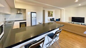 A modern kitchen with a central island, a dining area with a TV, and a painting on the wall. - Phillip Island Towers (Cowes)