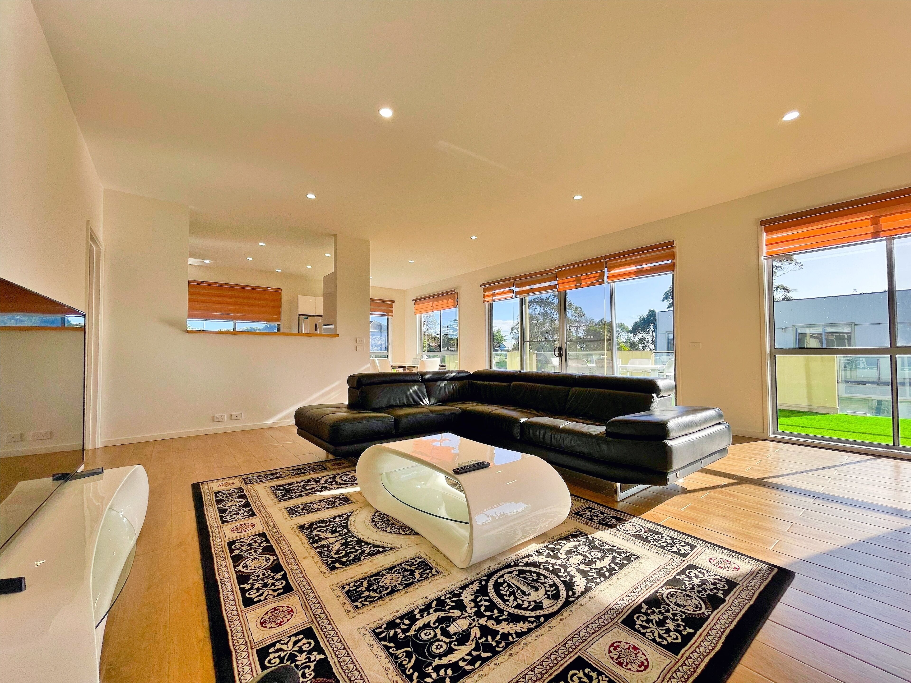 A spacious living room with a black leather sofa, a glass coffee table, and a patterned rug.