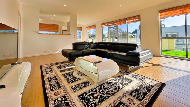 A spacious living room with a black leather sofa, a glass coffee table, and a patterned rug. - Phillip Island Towers (Cowes)
