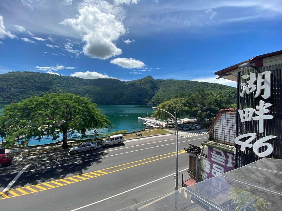 A road with parked cars, a boat docked by the water, and a building with a sign.