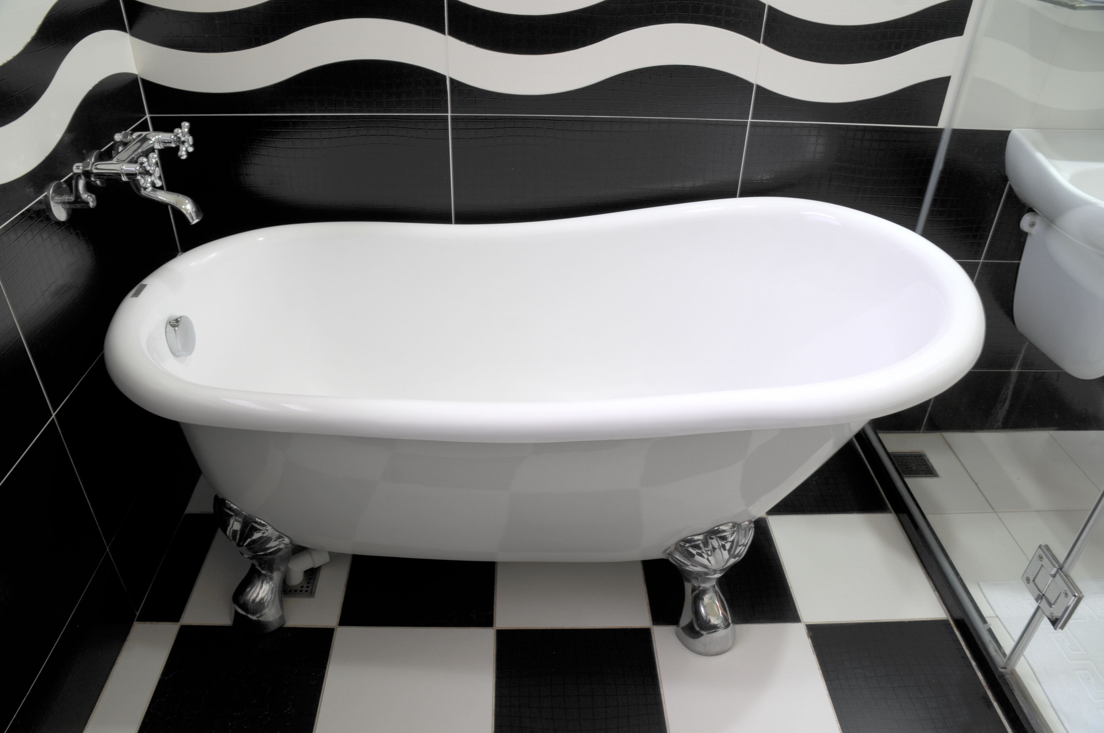 A bathroom with a white freestanding bathtub, black and white checkered floor tiles, and black and white wavy wall tiles.