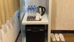 A compact kitchenette with a coffee maker, water bottles, a kettle, and a small refrigerator. - Sunny Hotel (Taipei)