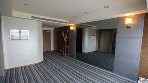 A hotel corridor with patterned carpet, a wooden bench, and wall-mounted lights. - Sunny Hotel (Taipei)
