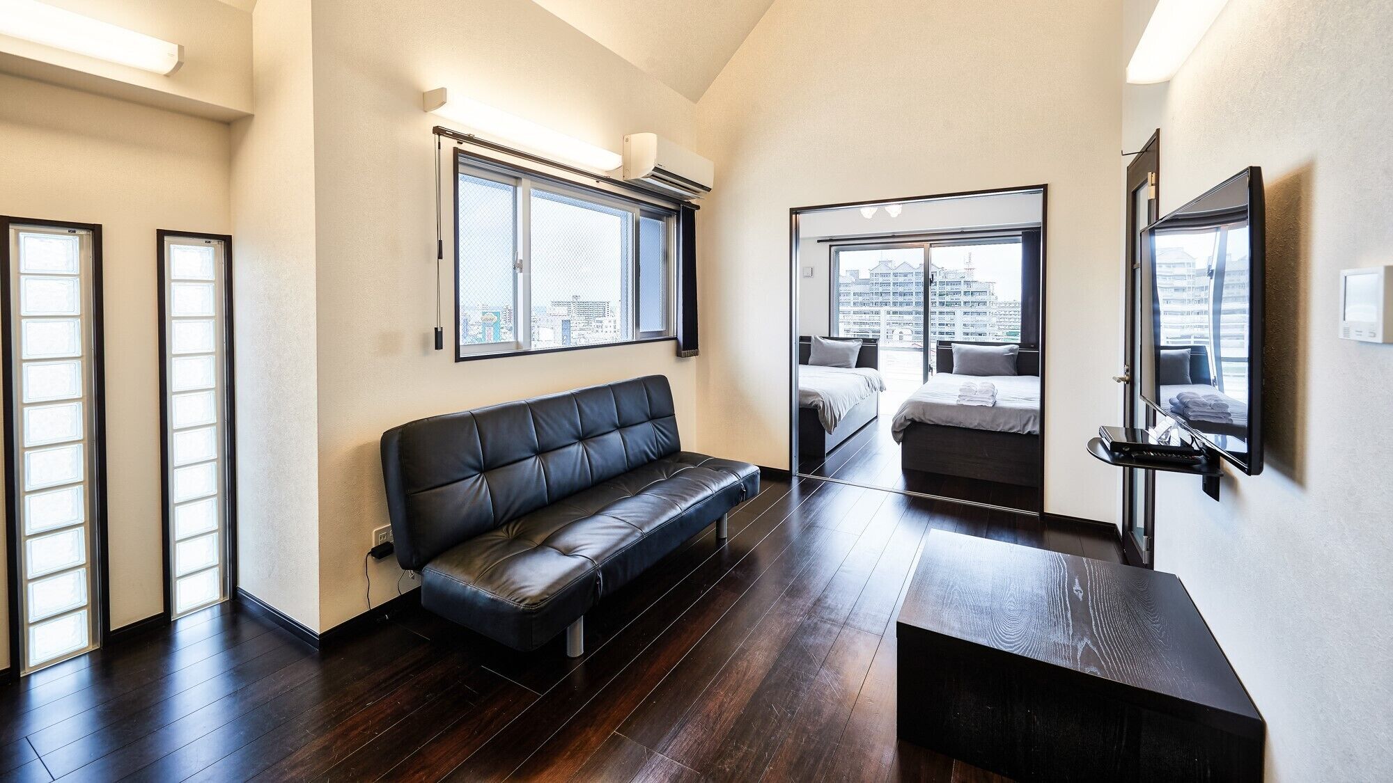 Ein modernes Hotelzimmer mit einer Ledersofa, einem Bett, einem Fernseher und großen Fenstern mit Blick auf die Stadt.