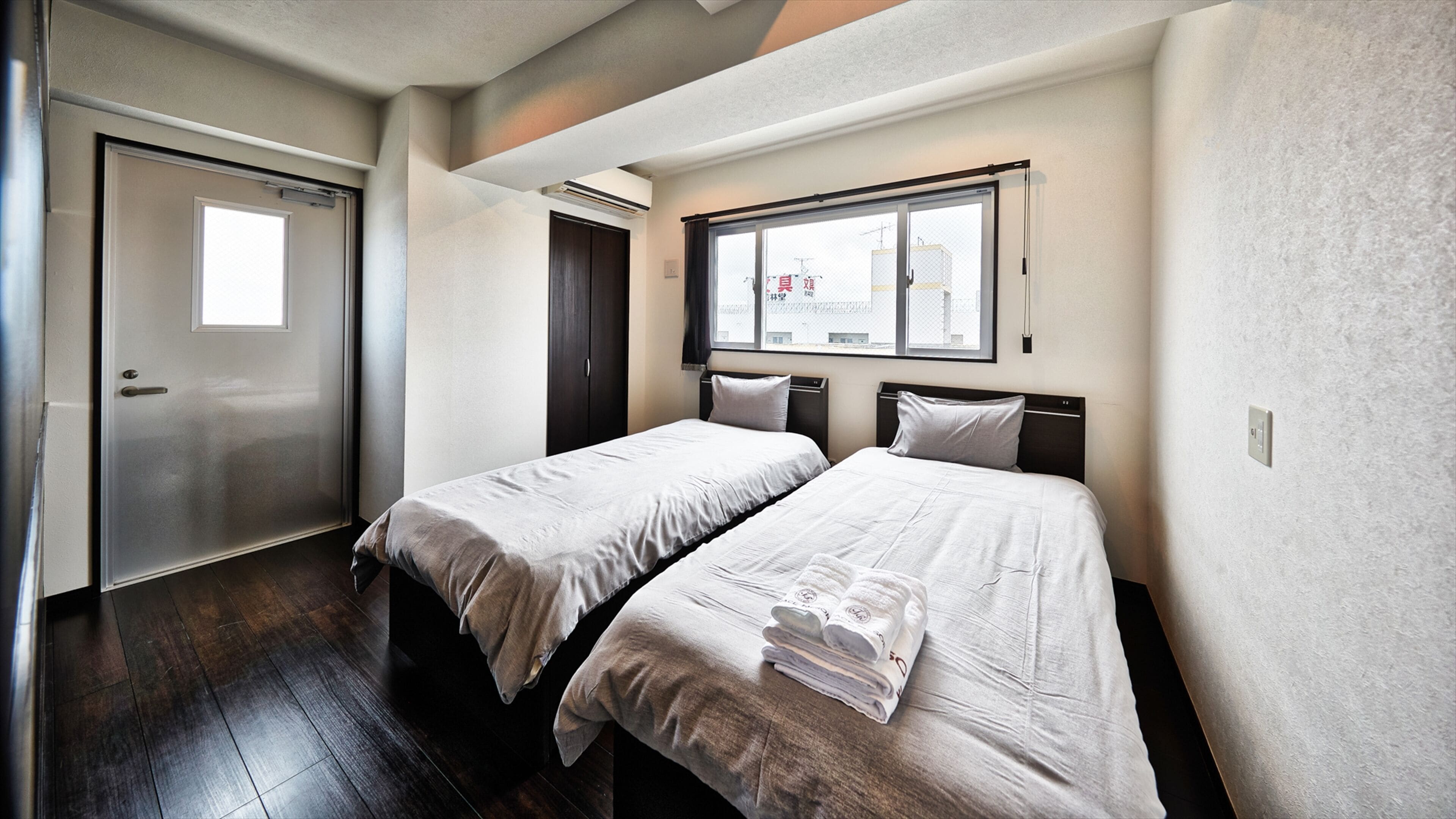 A hotel room with two beds, a window with a view, and a door.