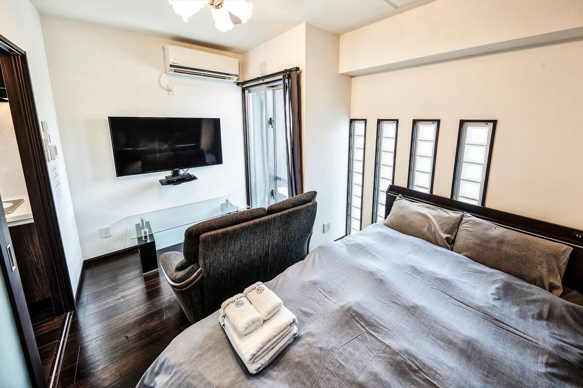 Une chambre d’hôtel avec un lit, un téléviseur fixé au mur, une fenêtre avec des rideaux et un plancher en bois.