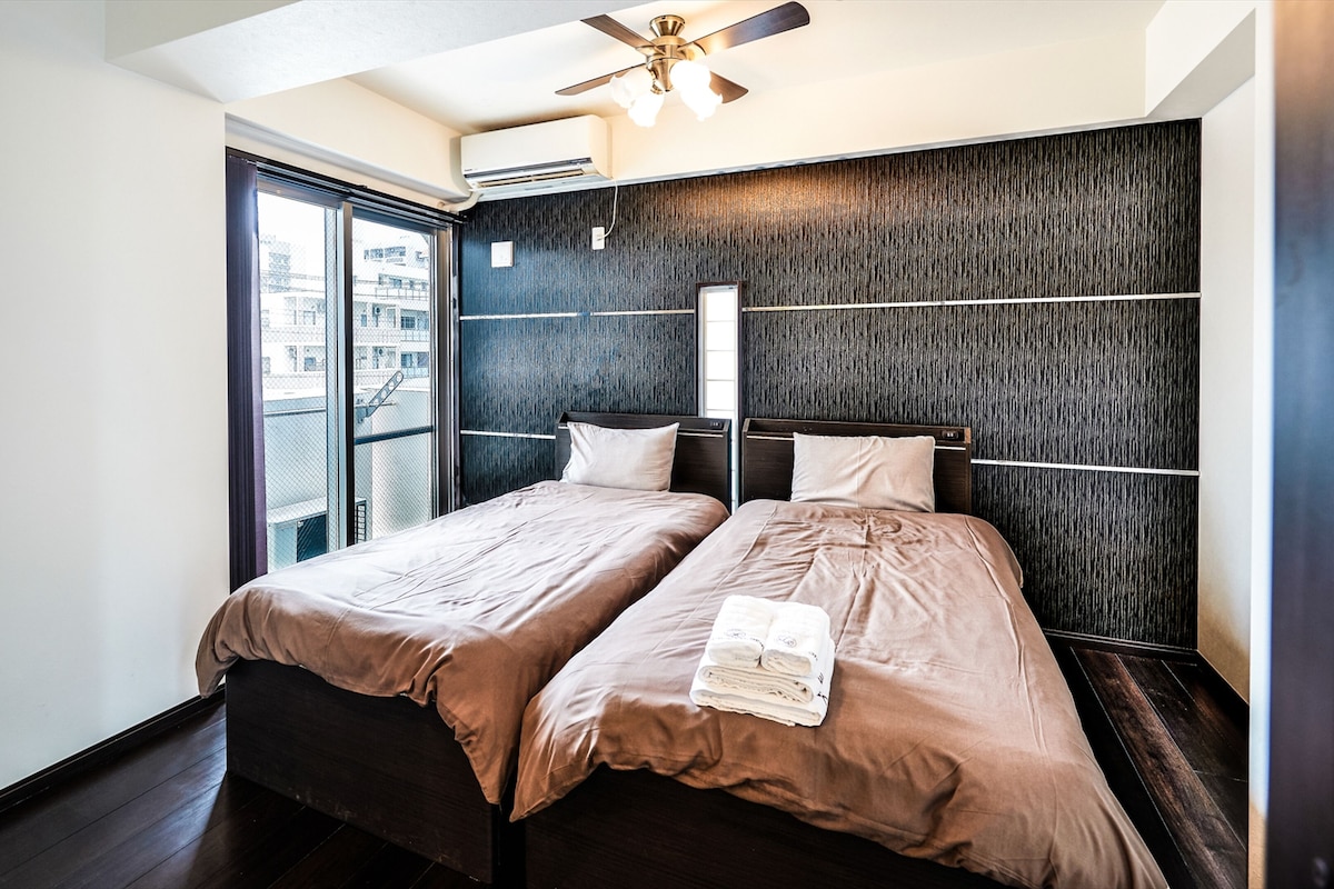 Una habitación de hotel moderna con dos camas, un ventanal grande y un ventilador de techo.