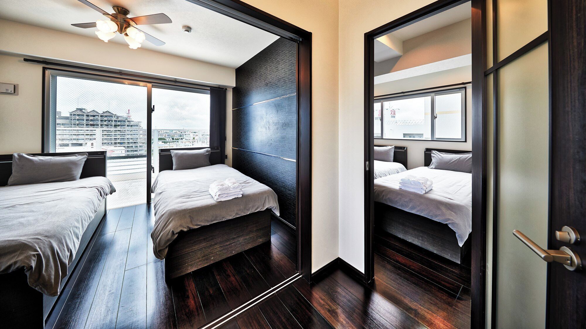 Ein Hotelzimmer mit zwei Betten, einem Deckenventilator und Blick auf die Stadtlandschaft.