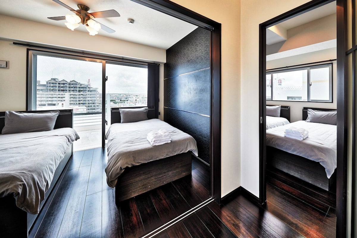 Quarto de hotel com duas camas, um ventilador de teto e vista para a cidade.