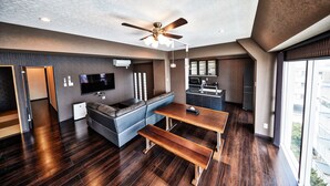A modern living room with a sofa, a TV, a ceiling fan, and a dining table. - Terrace Resort Shintoshin (Naha)