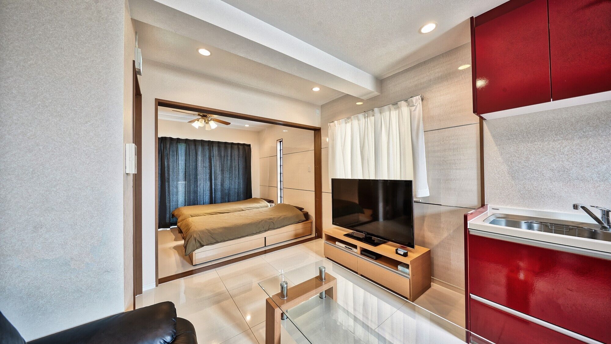A modern hotel room with a bed, TV, and kitchenette.