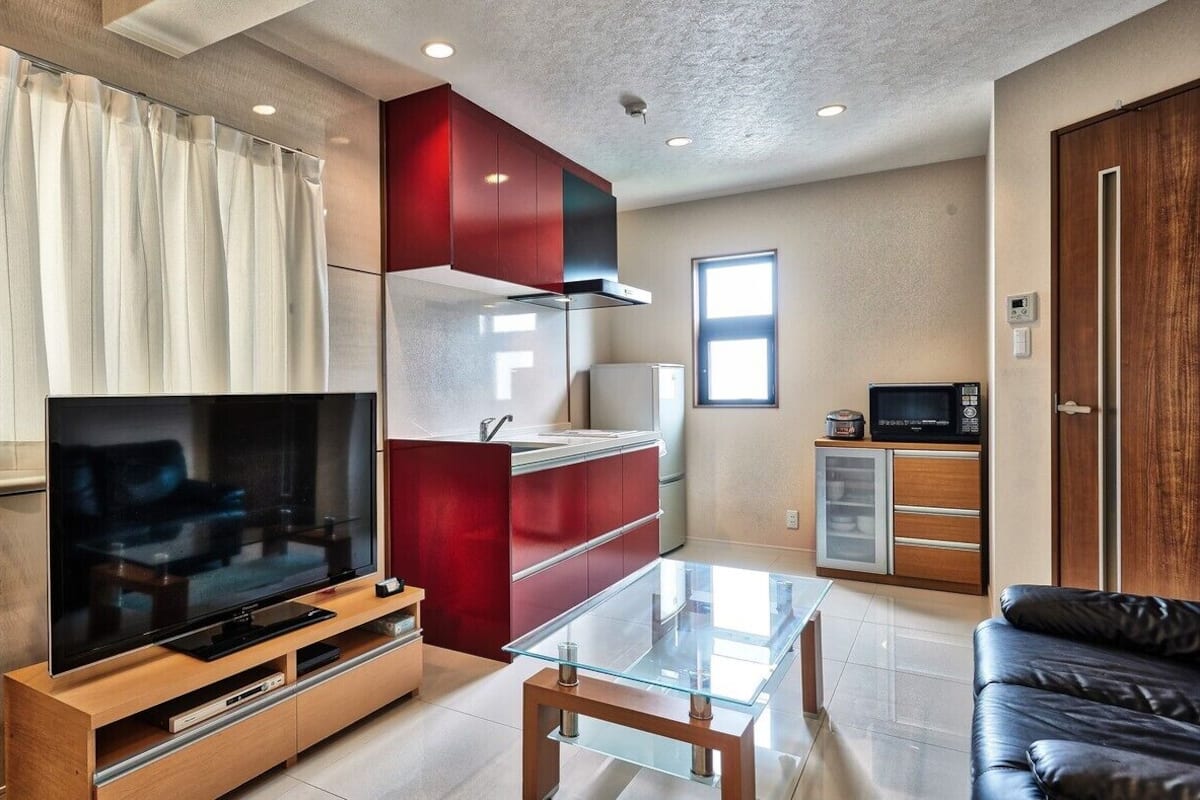 Una sala de estar moderna con un televisor de pantalla plana, una mesa de centro de vidrio, un mueble rojo y un sofá de cuero negro.