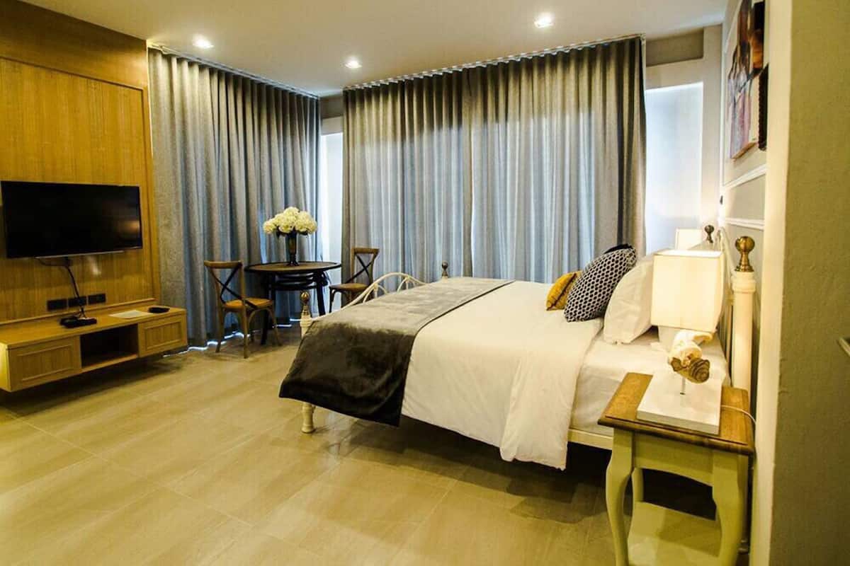 A modern hotel room with a large bed, a TV, a desk with a chair, and a small table with a lamp.