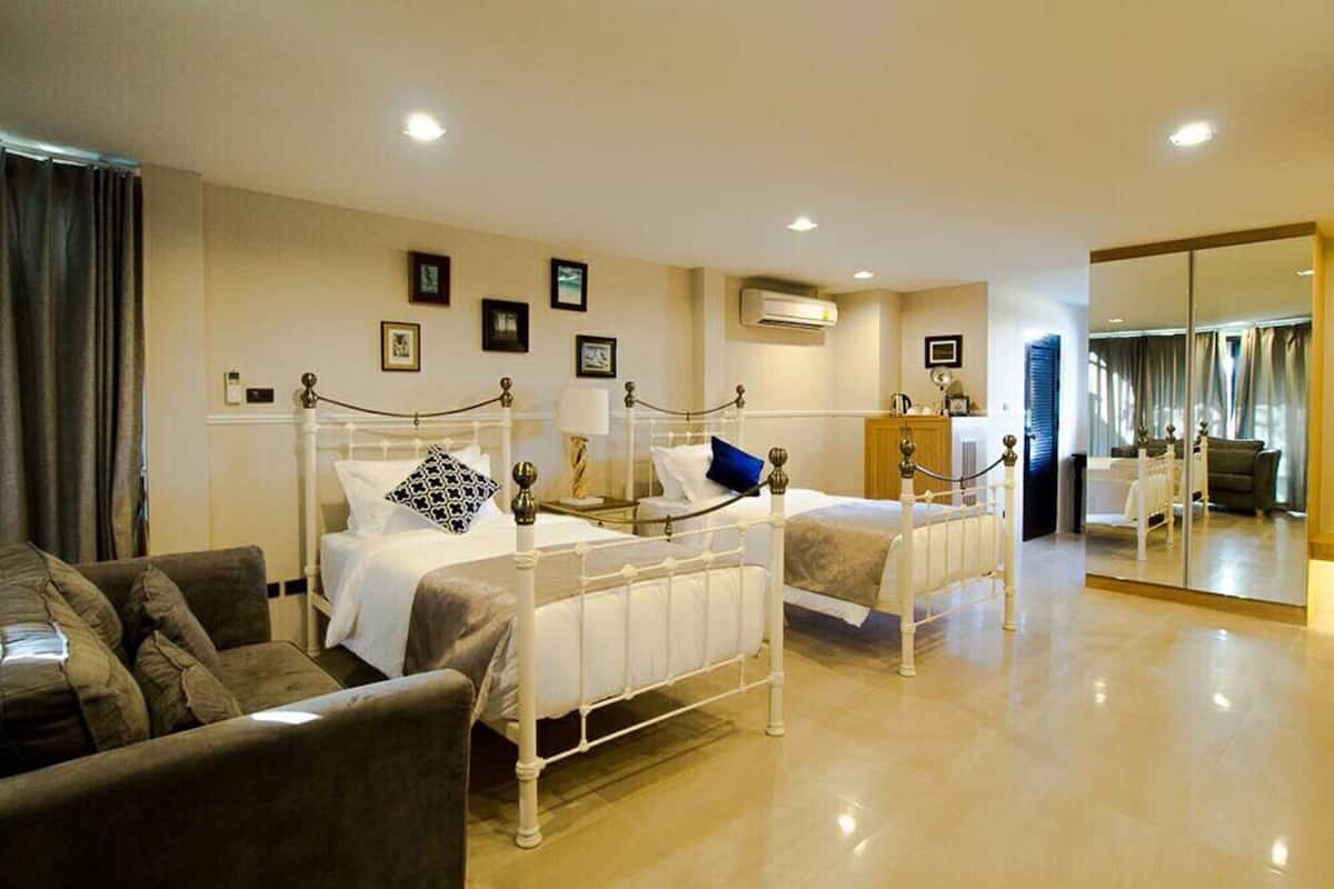 A hotel room with two beds, a sofa, a mirror, and a large window.
