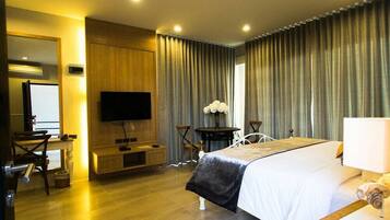 Habitación de hotel con cama, escritorio con silla, televisión y un amplio ventanal con cortinas.