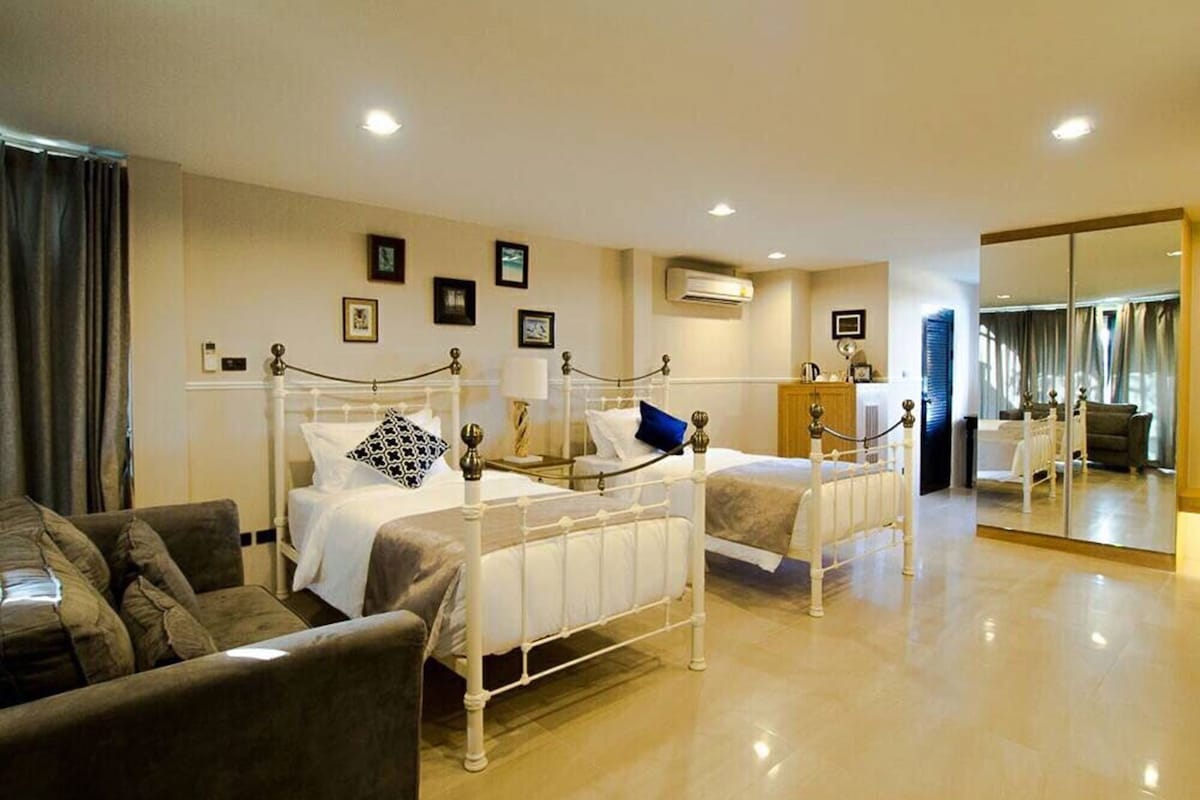 Habitación de hotel con dos camas, un sofá, un espejo y cuadros en la pared.