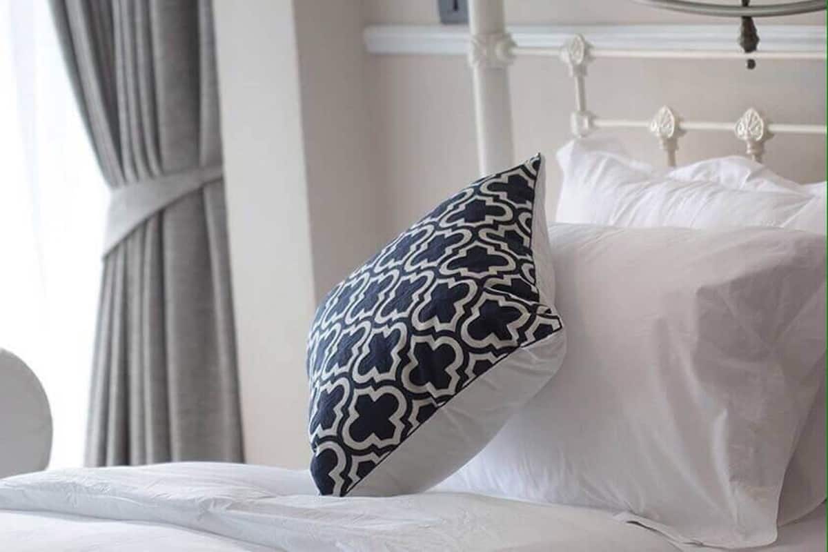 A bed with white bedding and a single patterned pillow.