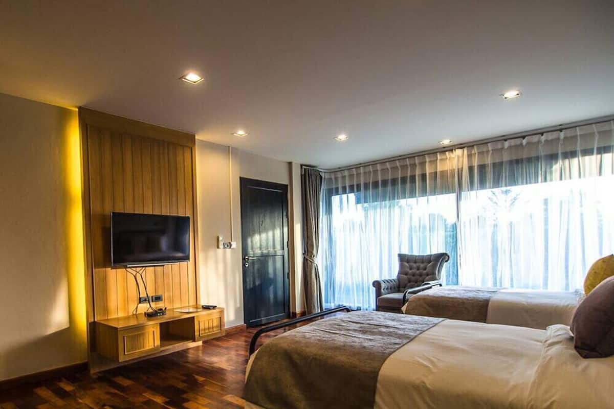 A hotel room with two beds, a TV, a wooden cabinet, and a large window with curtains.
