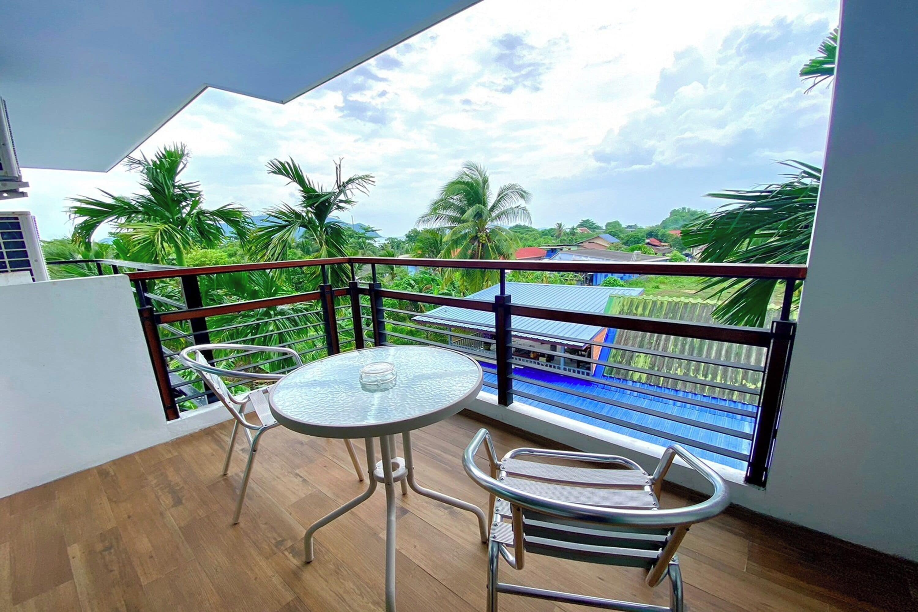 A balcony with a glass table and chairs, overlooking a pool and lush greenery.