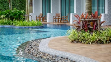 Une piscine entourée d’une terrasse en bois, de plantes tropicales et de chaises.