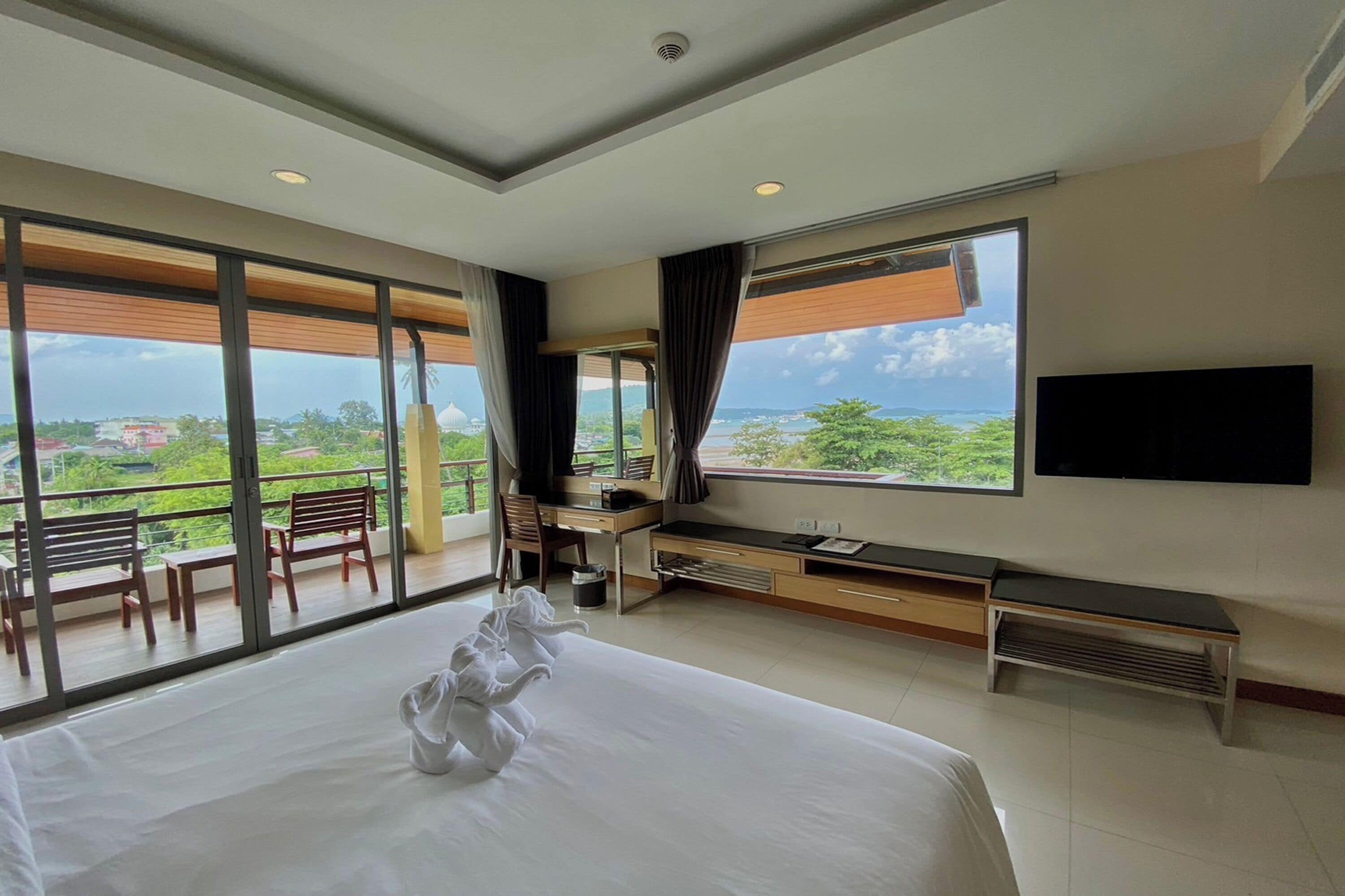 Quarto de hotel com cama grande, escrivaninha, cadeira, televisão e varanda com vista.