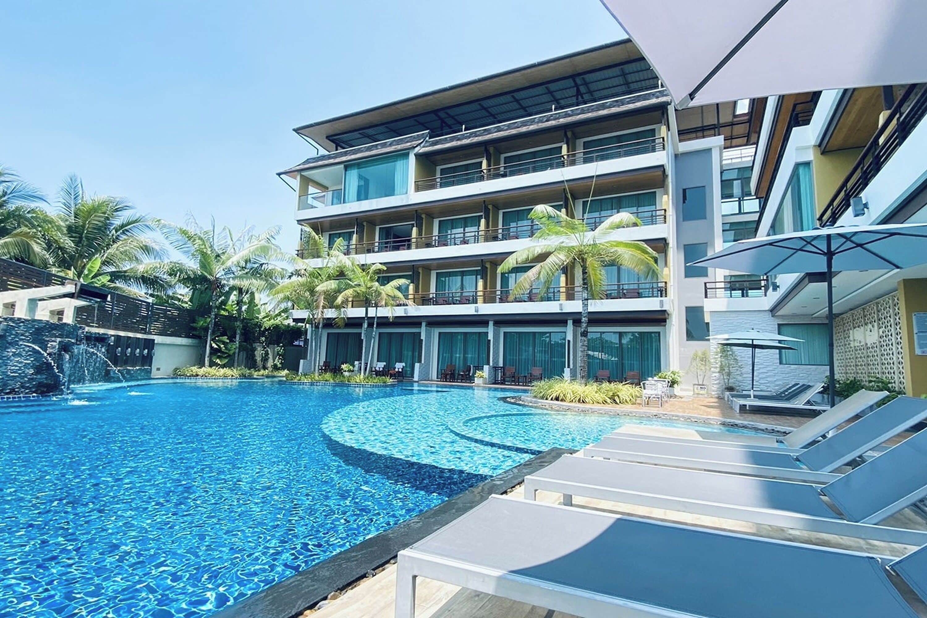 A modern hotel with a swimming pool, palm trees, and lounge chairs.