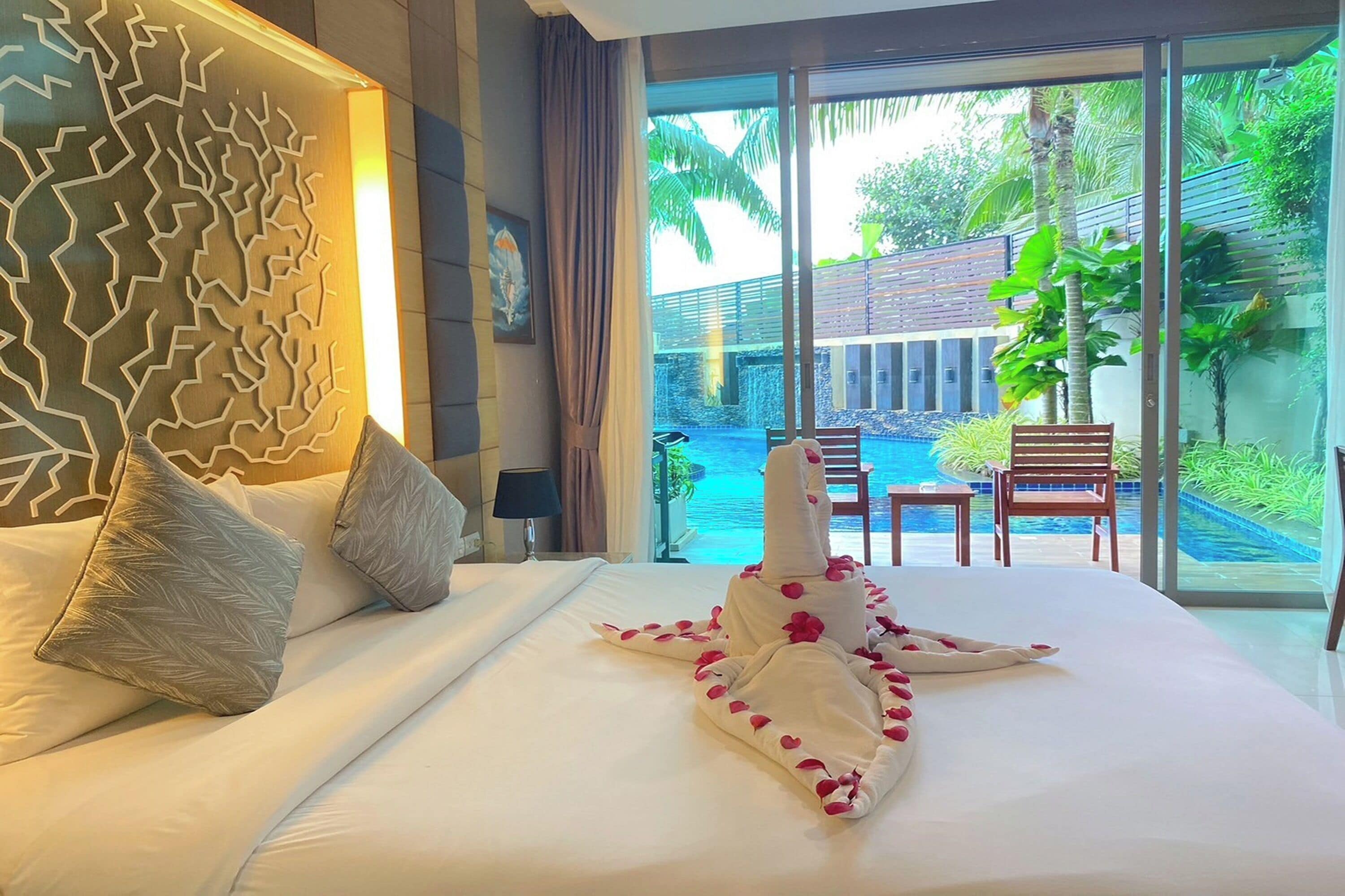 A hotel room with a large bed, a decorative wall, a view of a pool and outdoor seating area.