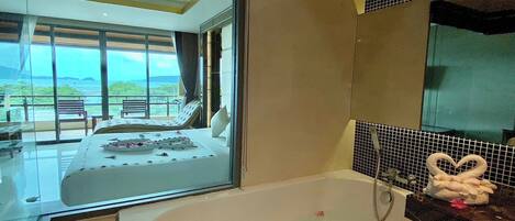 A modern bathroom with a bathtub, a large mirror, and a view of a balcony with a bed.