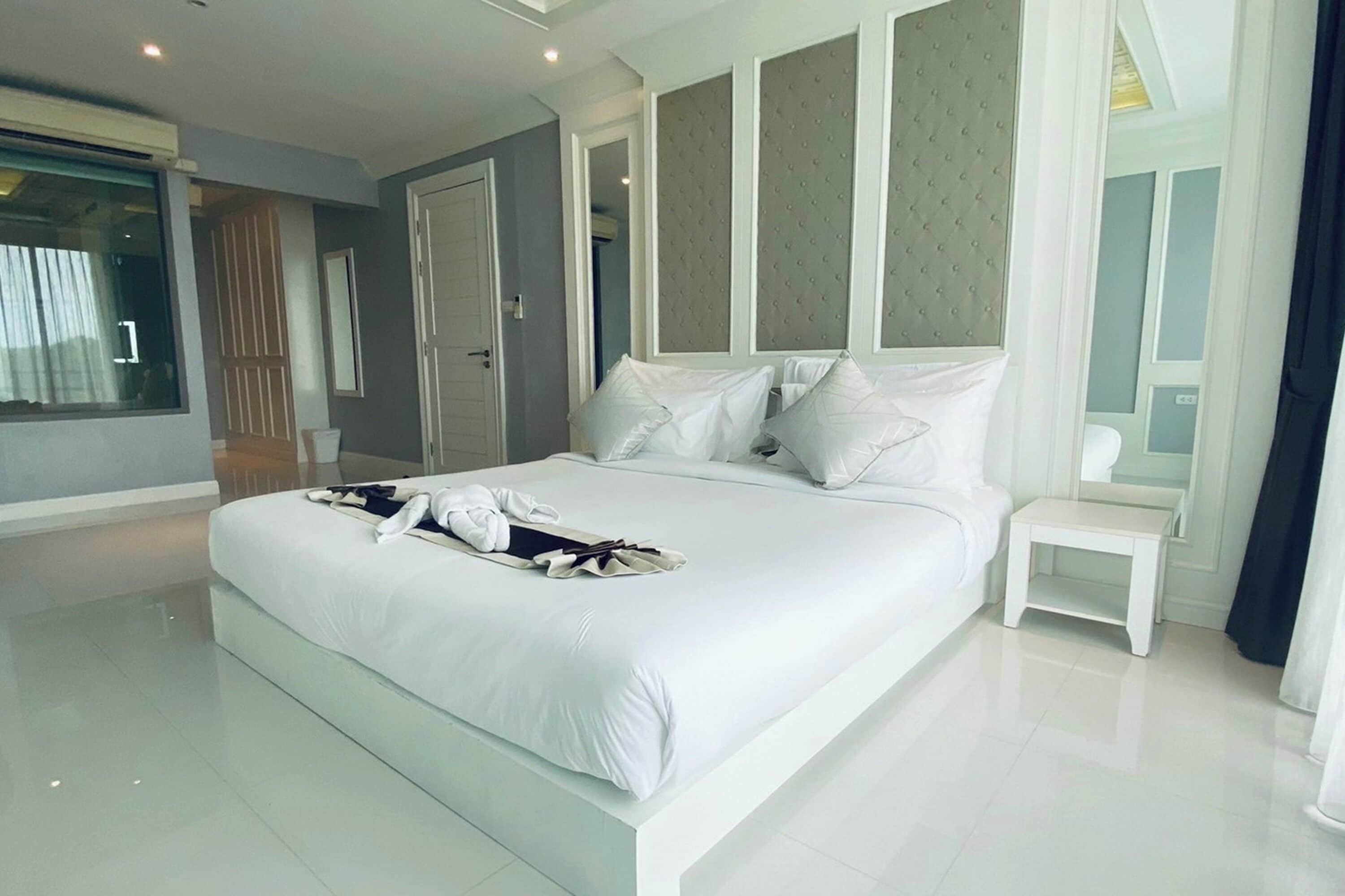 Una habitación de hotel moderna con una cama grande, una mesita de noche pequeña y un ventanal amplio.