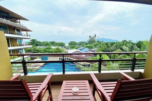 A balcony with wooden chairs and a table, overlooking a swimming pool and lush greenery. - Aqua Resort Phuket - Near Beach and Chalong Pier (Rawai)