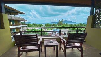 A balcony with two wooden chairs and a small table, overlooking a lush landscape with trees and distant mountains.